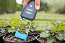 Hand using a soil tester on small plants in pots outdoors